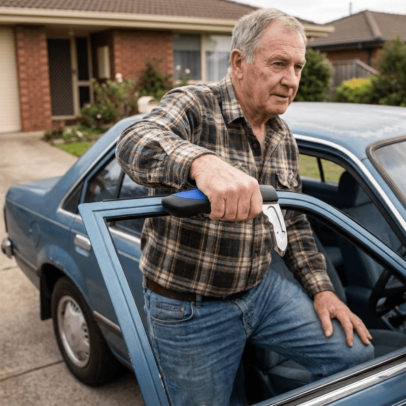 An older man in a brown and black plaid shirt and blue jeans stands next to the driver's seat of a blue vintage car, holding a car door assist handle in the one hand.